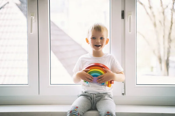 Kind Junge Auf Dem Hintergrund Des Fensters Hält Hölzerne Regenbogen — Stockfoto
