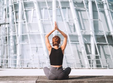 Yoga ve meditasyon modern şehirde. Kadının meditasyon yapması ve şehir binalarının arka planında nefes alma egzersizi yapması. Sağlıklı yaşam biçimi, şehir hayatı, rahatlama, stres yok.