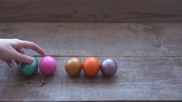 Uma mão feminina tomando ovos de Páscoa coloridos de mesa de madeira. Decorações de férias de Páscoa, fundo conceito de Páscoa — Vídeo de Stock