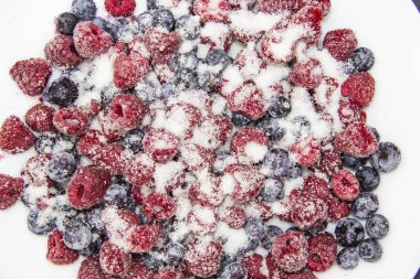 Donmuş ahududu ve yaban mersininden yapılmış böğürtlenli şeker karışımı. Şekerli Donmuş Böğürtlen. Donmuş ahududu ve yaban mersinli tatlı bir arka plan. Şekerli böğürtlenler arkada. Sağlıklı bir dut.