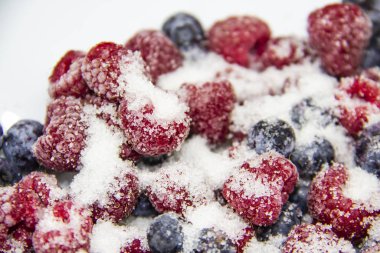 Donmuş ahududu ve yaban mersininden yapılmış böğürtlenli şeker karışımı. Şekerli Donmuş Böğürtlen. Donmuş ahududu ve yaban mersinli tatlı bir arka plan. Şekerli böğürtlenler arkada. Sağlıklı bir dut.