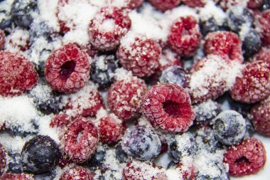 Donmuş ahududu ve yaban mersininden yapılmış böğürtlenli şeker karışımı. Şekerli Donmuş Böğürtlen. Donmuş ahududu ve yaban mersinli tatlı bir arka plan. Şekerli böğürtlenler arkada. Sağlıklı bir dut.