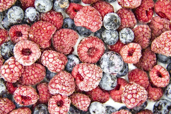 A Berry mix from frozen raspberries and blueberries. A Frozen Berries from freezer.  A sweet background with frozen raspberries and blueberries.   A heathy Berries in the background.