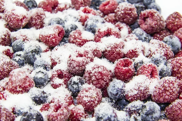 A Berry mix in sugar from frozen raspberries and blueberries. A Frozen Berries with Sugar.  A sweet background with frozen raspberries and blueberries. Sugar Berries in the background.  A heathy berry