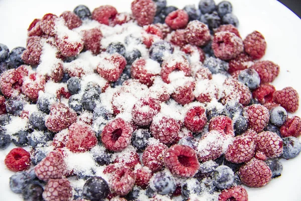 A Berry mix in sugar from frozen raspberries and blueberries. A Frozen Berries with Sugar.  A sweet background with frozen raspberries and blueberries. Sugar Berries in the background.  A heathy berry