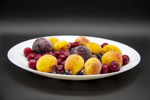 A Berry mix from frozen currant, apricot, plum, cherry on the white plate. Frozen Berries from freezer. A background with frozen plum, currant, apricot and cherry. A healthy Berries on the background