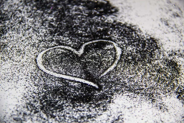 A black glitter on the white background.  A heart painted on the black sand