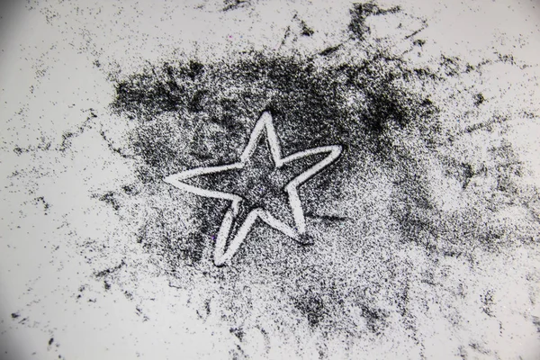 A black glitter on the white background. Star painted by black sand.