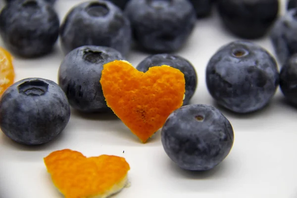 Fresh blueberry  with mandarin peel in form a heart on white background. A composition of the blueberries, mandarin peel which is organic and healthy. The berries full of vitamins.