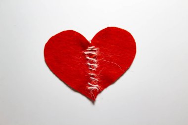 Kırık bir kalbi iplikle diktim. Keçeden yapılmış kırmızı kalp. Parçalanmış aşk konsepti. İplikle sabitlenmiş kalp.