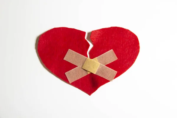 Broken heart and glued together with a band-aid. A heart from felt. A concept about broken love. Heart with plaster isolated on white background