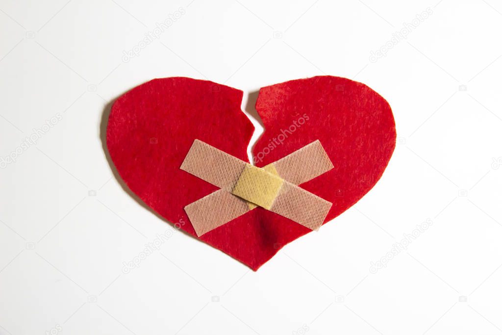 Broken heart and glued together with a band-aid. A heart from felt. A concept about broken love. Heart with plaster isolated on white background