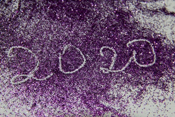 composition with purple sparkles and the inscription 2020. Purple glitter against background. Abstract and textured background