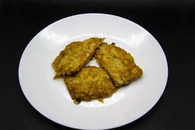 Siyah arka planda etli beyaz tabak. Tabakta yumurta içinde kızarmış et. Üç kızarmış pirzola.