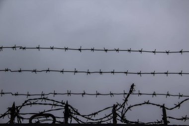 Gri gökyüzü arkaplanına dikenli teller geriliyor.