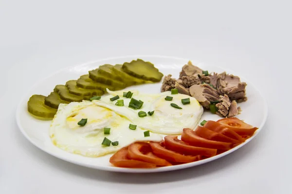 Delicious fresh tuna with eggs, tomatoes, cucmbers with green onion at the morning. Healthy and diet breakfast with tuna, eggs and vegetables on the white plate against white background
