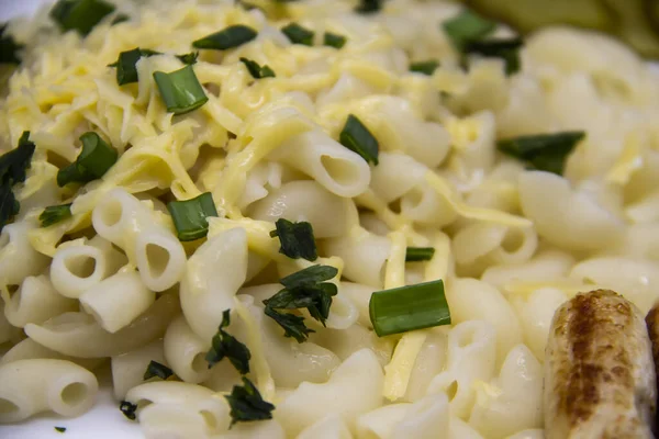 Pasta on a plate with cheese on top and green onions. Delicious pasta made from high quality flour with chicken sausage from grill and sliced cucumber from jar. Horns made of flour cooked with cheese, parsley, sausage,onion and sauce