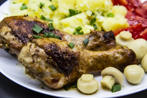 Tasty cooked chicken legs with potatoes, tomatoes, mushrooms on a white plate. Delicious potatoes with onion and dill on dinner, lunch. Amazing chicken legs cooked in spice. Ukrainian healthy meal
