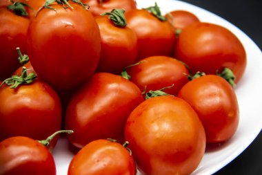 Beyaz bir tabakta koyu arka planda taze kırmızı domatesler. GDO 'suz güzel ve sağlıklı vişneli domatesler..