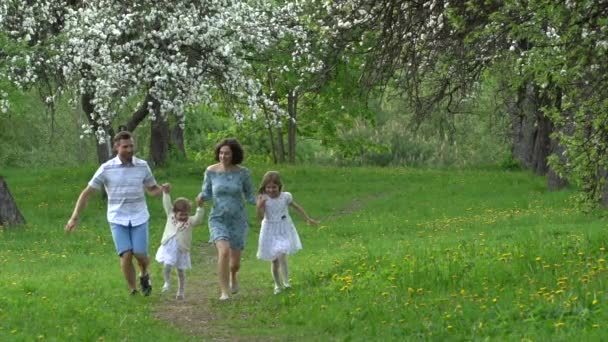 Genitori e figlie corrono nel parco primaverile in un giardino alberato fiorito. Rallentatore — Video Stock