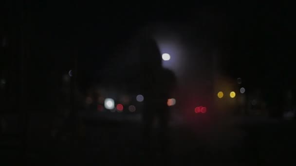 Silhouet van een man met een kap op 's nachts in een stad achtergrond — Stockvideo