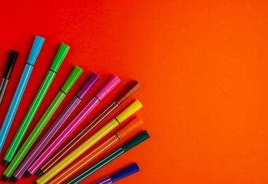 Parlak turuncu arka planda çok renkli keçeli kalemler.