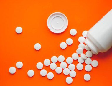 Parlak turuncu arka planda beyaz bir kavanozdan yayılmış beyaz haplar