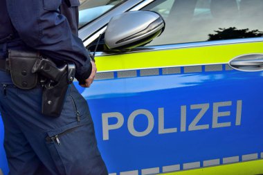 Alman polis arabasının yanında elinde cep telefonu olan bir polis..