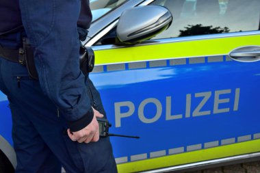 Alman polis arabasının yanında elinde cep telefonu olan bir polis..