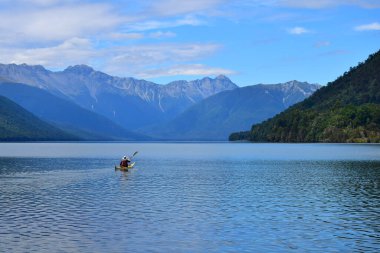 Sarı bir kanoyla Rotoroa Gölü 'nde kürek çeken bir adam. Arka planda dağlar. Nelson Lakes Ulusal Parkı, Tasman, Yeni Zelanda, Güney Adası.