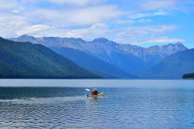 Sarı bir kanoyla Rotoroa Gölü 'nde kürek çeken bir adam. Arka planda dağlar. Nelson Lakes Ulusal Parkı, Tasman, Yeni Zelanda, Güney Adası.