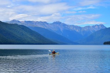 A man in a yellow canoe paddling across Lake Rotoroa. Mountains in the background. Nelson Lakes National Park, Tasman, New Zealand, South Island. clipart