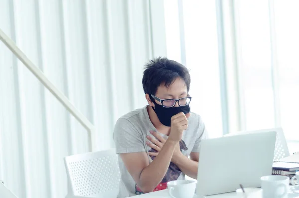 Asian Men Wearing Glasses Wearing a black mask Is working.A sick man sitting at work.In the white office there was a man in there.