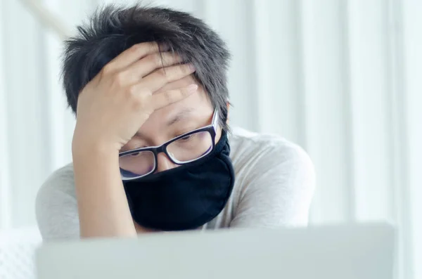 Asian Men Wearing Glasses Wearing a black mask Is working.A sick man sitting at work.In the white office there was a man in there.