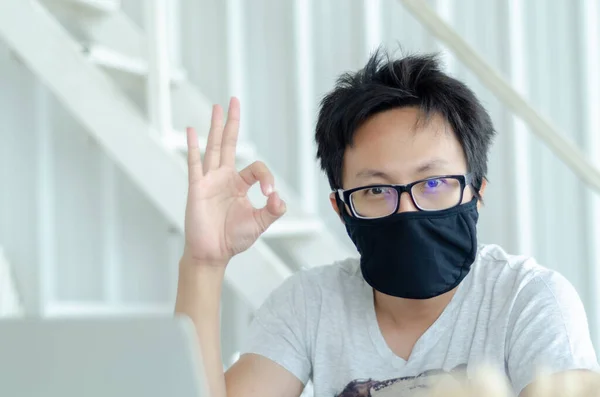 Asian Men Wearing Glasses Wearing a black mask Is working.A sick man sitting at work.In the white office there was a man in there.