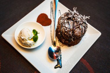 Kek, dondurma, çikolata. Vanilyalı çikolatalı çikolatalı kek ve beyaz tabakta çikolata şurubu. Seçici odaklanma, tonlama. Çikolata aromalı tatlı..