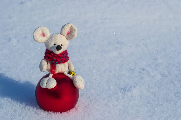 Christmas toy mouse, symbol of the year. In a red knitted scarf with a Christmas red ball. Against the background of white snow. Space for text