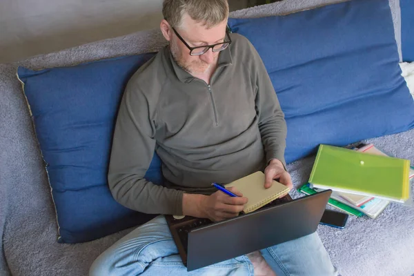 Şirketin bir çalışanı rahat giysiler içinde uzaktan çalışıyor, bir kanepede oturuyor. Evde internet üzerinden çalışmak, Coronavirus krizi sırasında uzaktan çalışmak. Seçici odak.