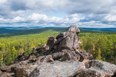 Büyük kayalardan yapılmış bir kayanın zirvesi. Orman vadisinin arka planında ve bulutlu mavi gökyüzünde. Metin için boşluk.