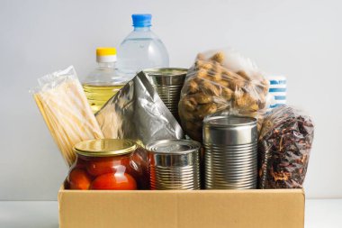 Bağış için kutuda yiyecek var. Konserve yemek, makarna, salamura domates, sebze yağı, su, çay, fıstık. Kağıt peçete. Yiyecek teslimatı ya da gıda bağışı konsepti. Coronavirus karantinası.
