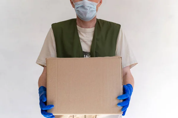 Üniformalı teslimatçı. Tıbbi koruyucu eldivenler ve maske içinde bir karton kutu tutuyor. Hızlı ve ücretsiz taşıma. Çevrimiçi alışveriş ve hızlı teslimat.