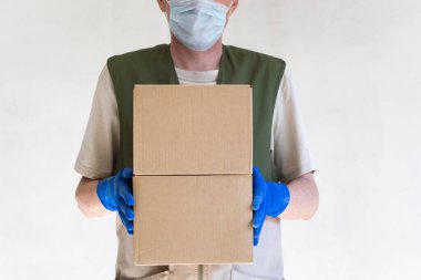 Üniformalı teslimatçı. Tıbbi koruyucu eldivenler ve maske içinde karton kutular tutuyor. Hızlı ve ücretsiz taşıma. Çevrimiçi alışveriş ve hızlı teslimat. Boşluğu kopyala