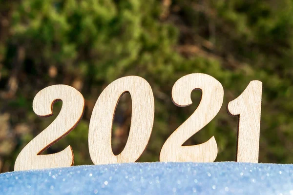 2021 yılını kutluyoruz. 2021 numaralı ahşap, karlı ve doğal bir yüzeyde. Parlak güneş tarafından bir ladin ormanının arka planına karşı aydınlatılmış. Doğal stil.