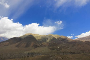 Kahverengi dağlar mavi gökyüzüne karşı beyaz bulutlarla