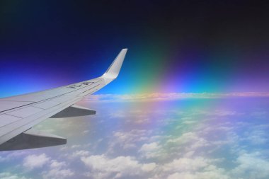 Uçak penceresinden bir kanat, bulutlar ve gökkuşağının görüntüsü