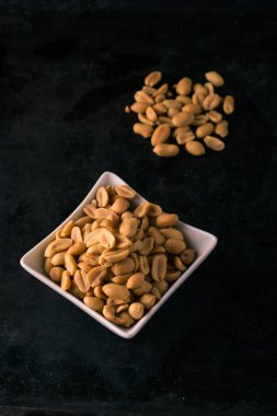 Tuzlu fıstık yığın üzerinde ve beyaz kase ile karanlık tepsi