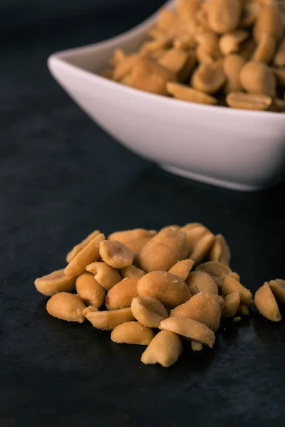 Haufen gesalzener Erdnüsse auf dunklem Tablett vor der Schüssel — Stockfoto