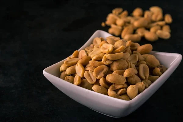 White square bowl full of salted peanuts on dark tray — Stock Photo, Image