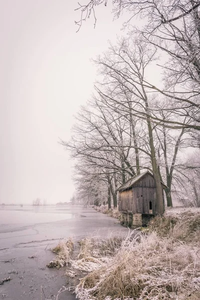 在雾蒙蒙的日子里, 冰冻的池塘旁的孤独的木屋 — 图库照片