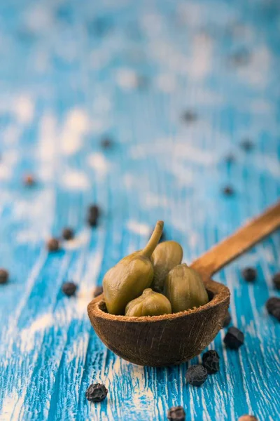 Paar kappertjes in houten lepel op een blauw bord — Stockfoto